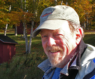 photograph of john copley, the artist, standing in wooded area with red buildings in the background